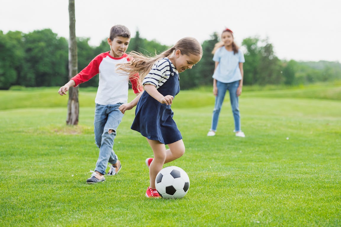 un garçon et deux filles jouant au foot sur une pelouse verte