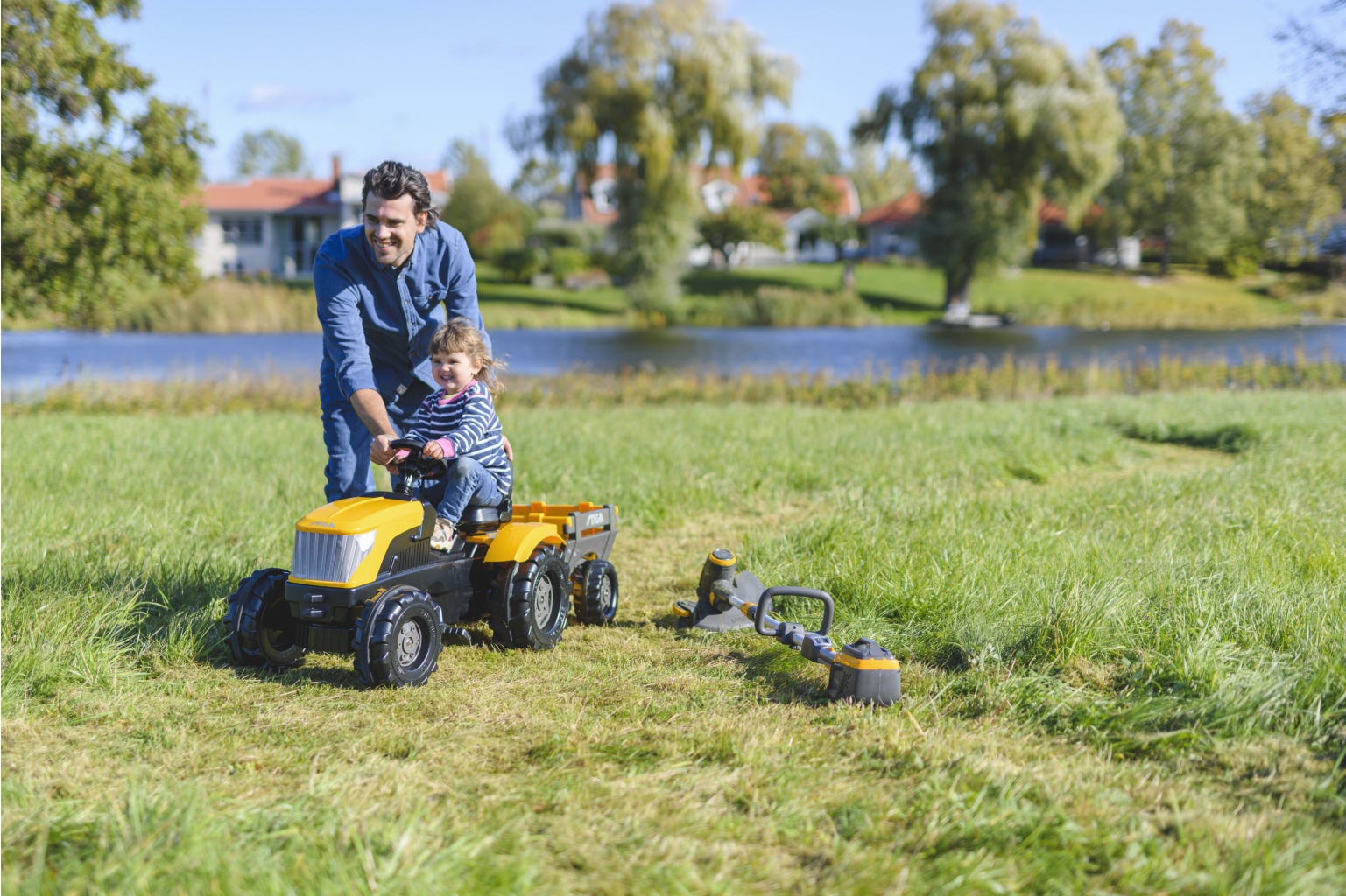Dad and daughter playing in the garden with a yellow toy tractor