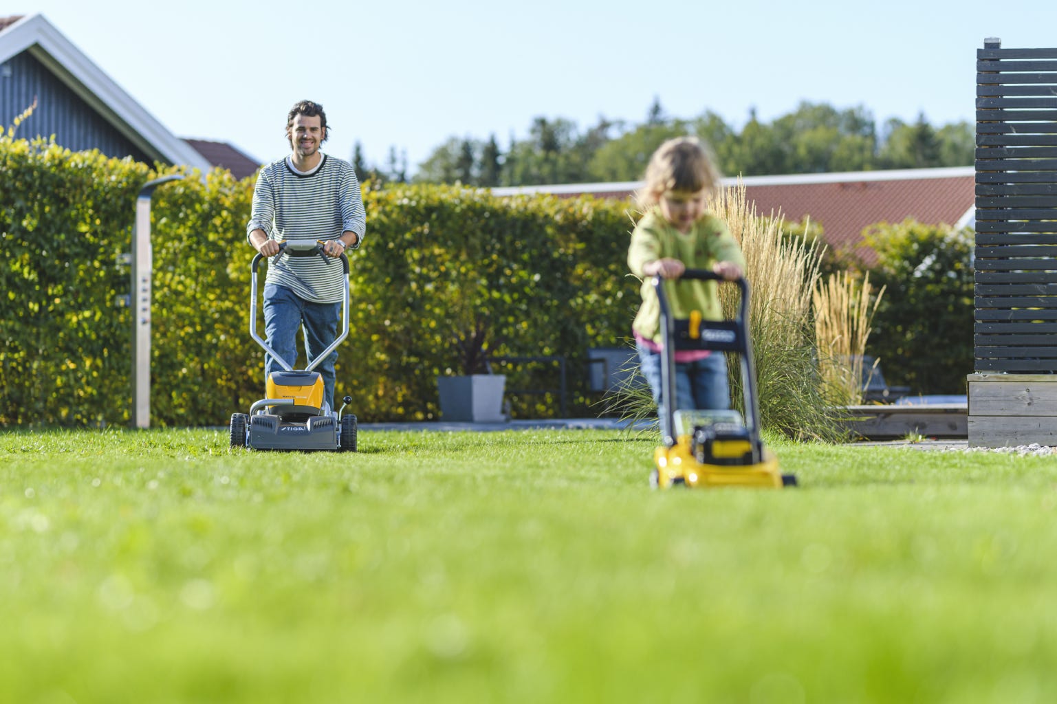 Dad and daughter mowing the lawn with battery lawn mower and yellow toy