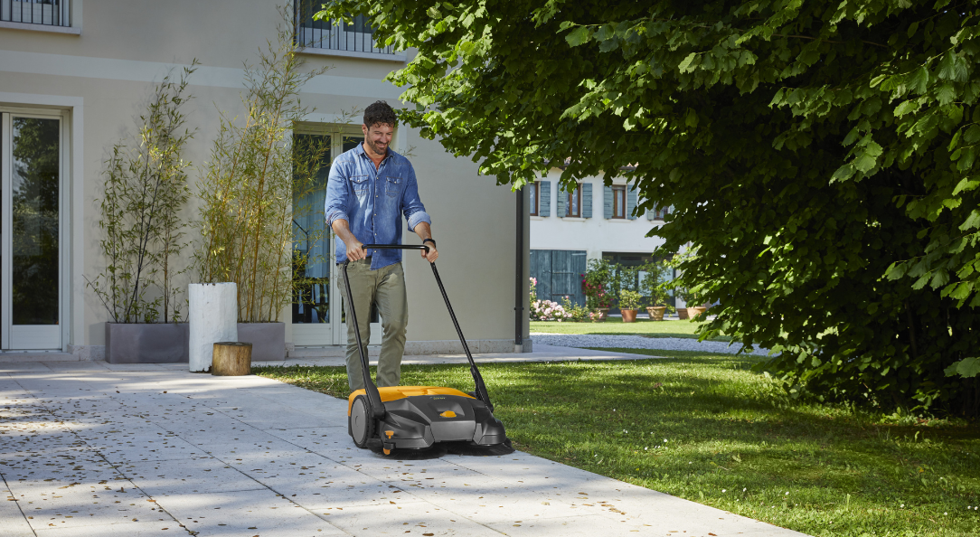 Man using STIGA sweeper to clear leaves on patio