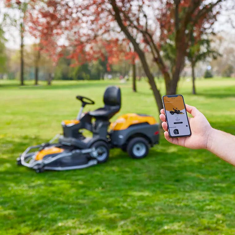 Händer håller en Smartphone och trycker på skärmen med en STIGA Park åkgräsklippare i bakgrunden