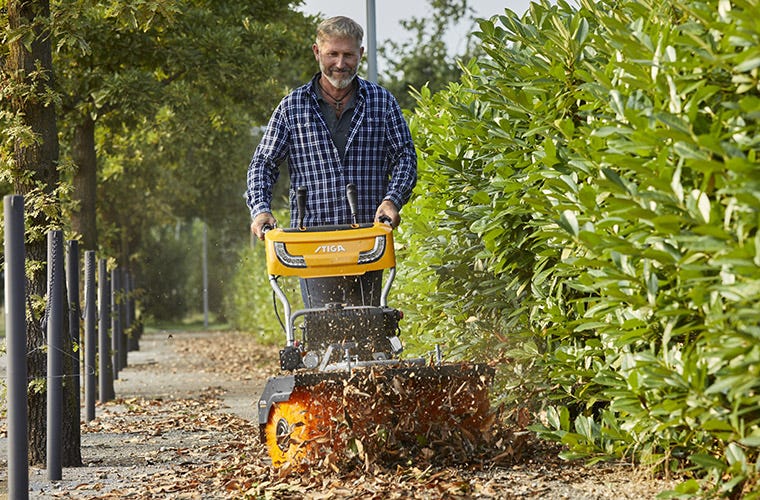 Man using STIGA sweeper to clean walkway from autumn leaves
