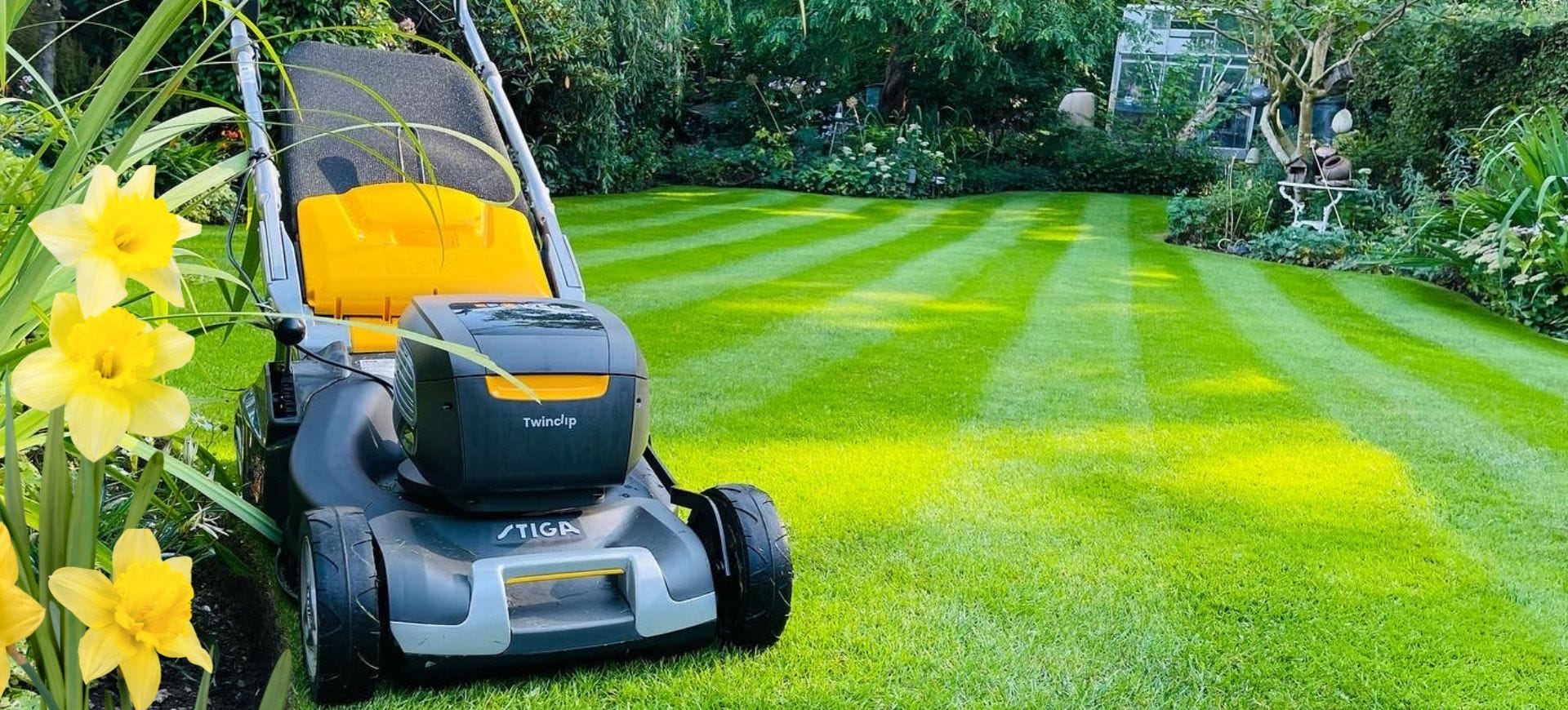 stiga lawnmower on a lovely striped lawn with spring flowers
