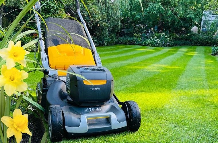 stiga lawnmower on a lovely striped lawn with spring flowers