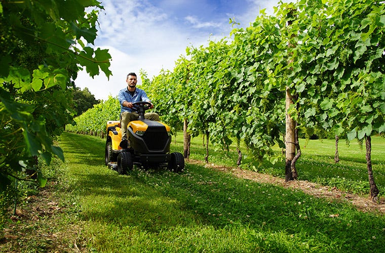 side view of a man riding a battery tractor in a vineyard